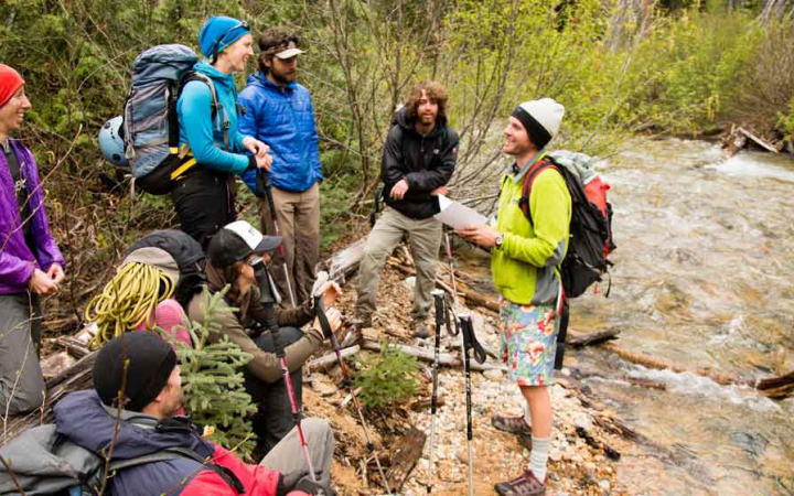 an instructor gives direction to a group of mountaineering students beside a river